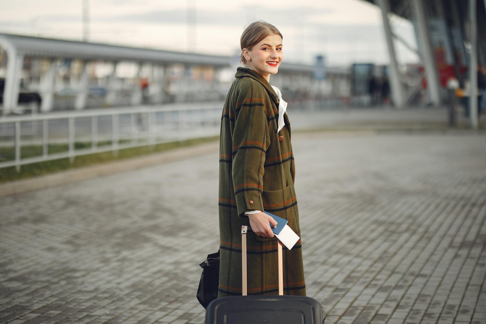 smiling female traveler walking with suitcase and passport near train station